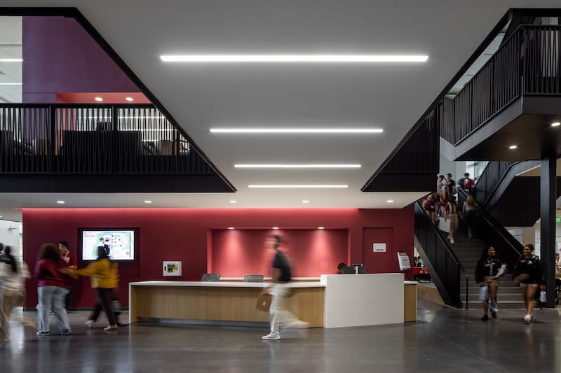 View of FSU Student Union lobby with welcome counter with a red accent wall behind it and a large staircase.