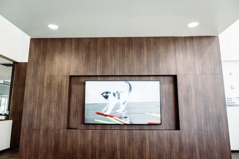 Flat screen TV mounted to a large wooden accent wall. The wall has a sleek rectangular indent in the center, housing the TV which displays a kitten playing with a toy.