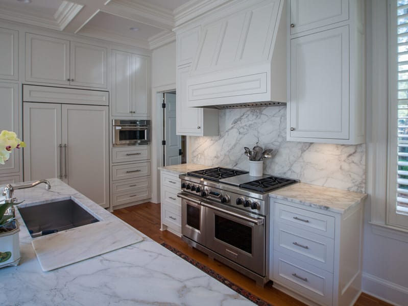 Stainless steel kitchen stove surrounded by cabinetry and matching range hood.