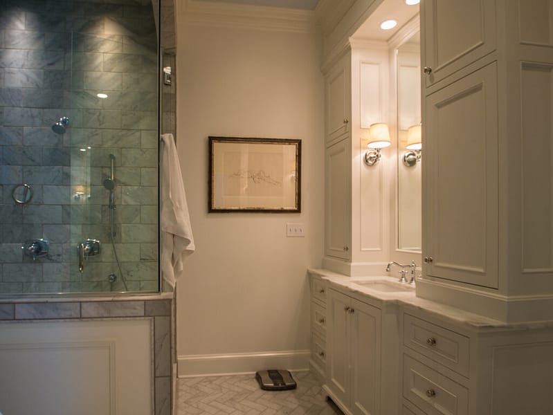 White bathroom vanity marble countertop and custom cabinetry next to a walk-in shower with stone walls.